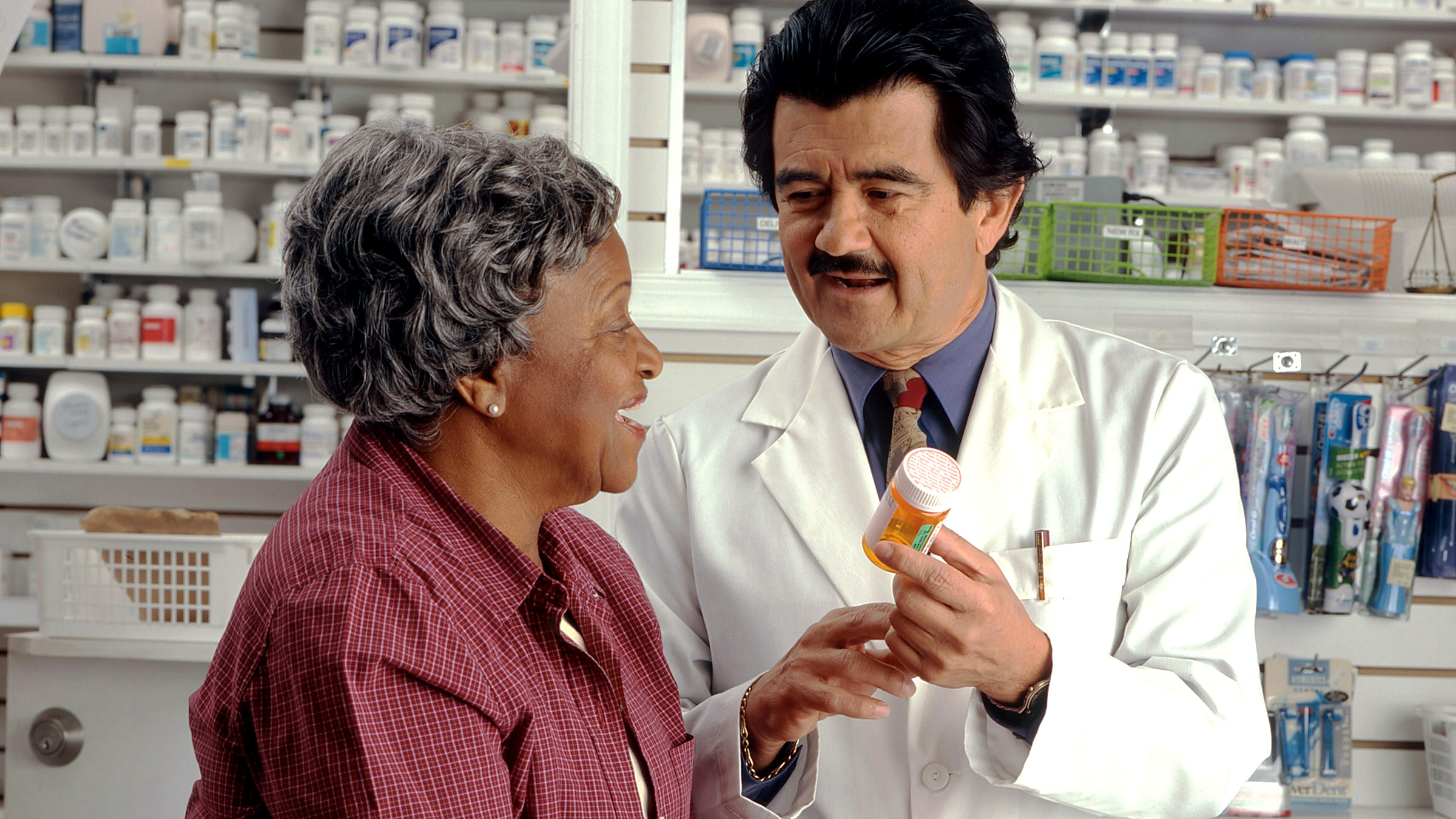 A pharmacist going over a prescription with an older customer at the counter